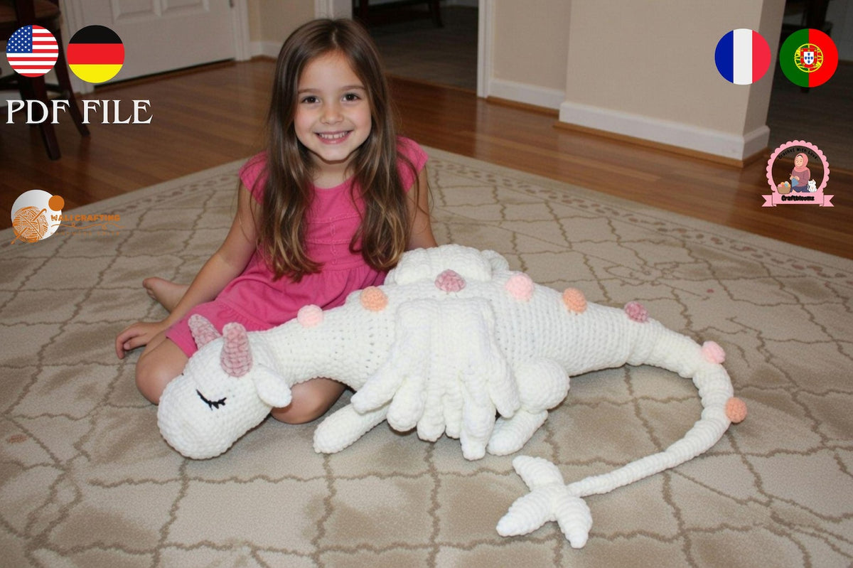 Little girl sitting next to giant sleeping white crochet unicorn dragon showing full size